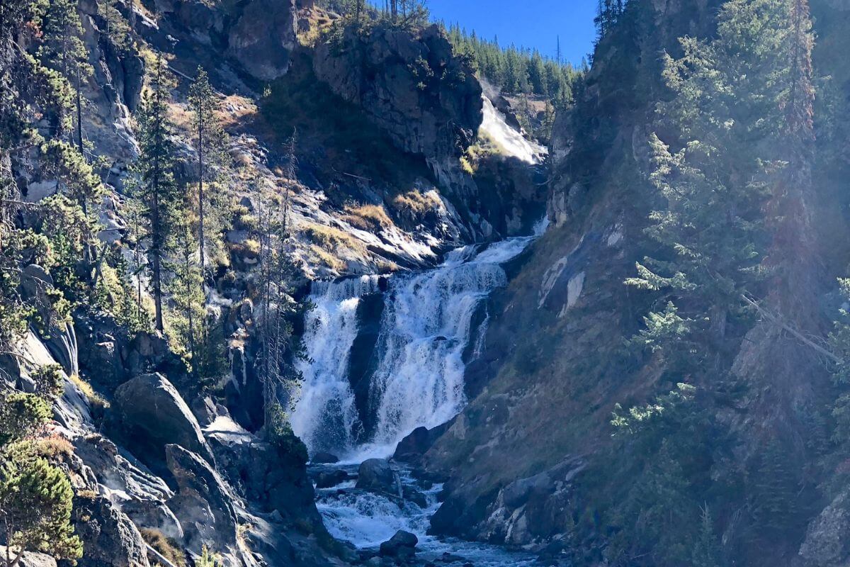A waterfall cascades through rocky, wooded terrain in the Montana mountains.
