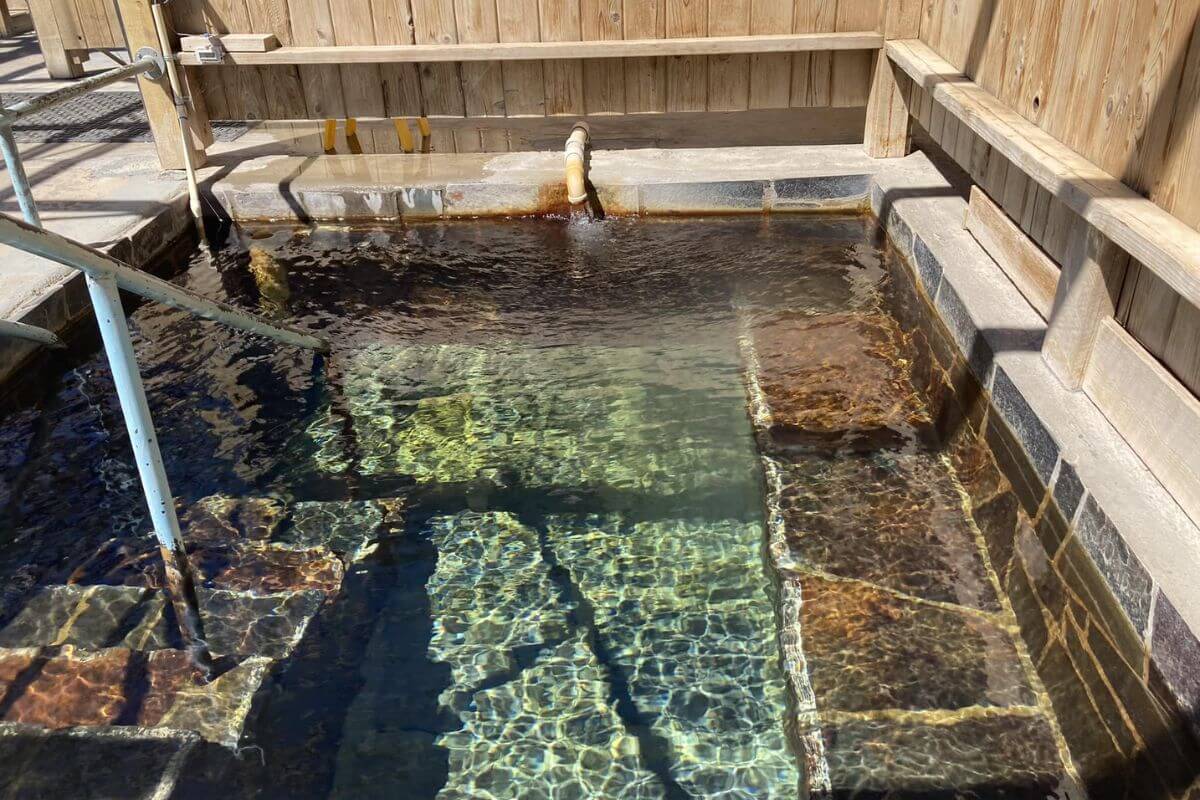 An outdoor hot spring pool with stone edges and clear waters, surrounded by a wooden fence, at Wild Horse Hot Springs.