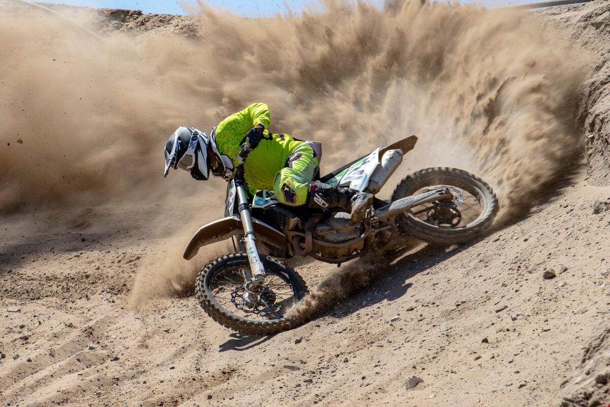 A man on a dirt bike skillfully navigates a sharp turn, sending sand flying, during a Montana dirt bike tour.