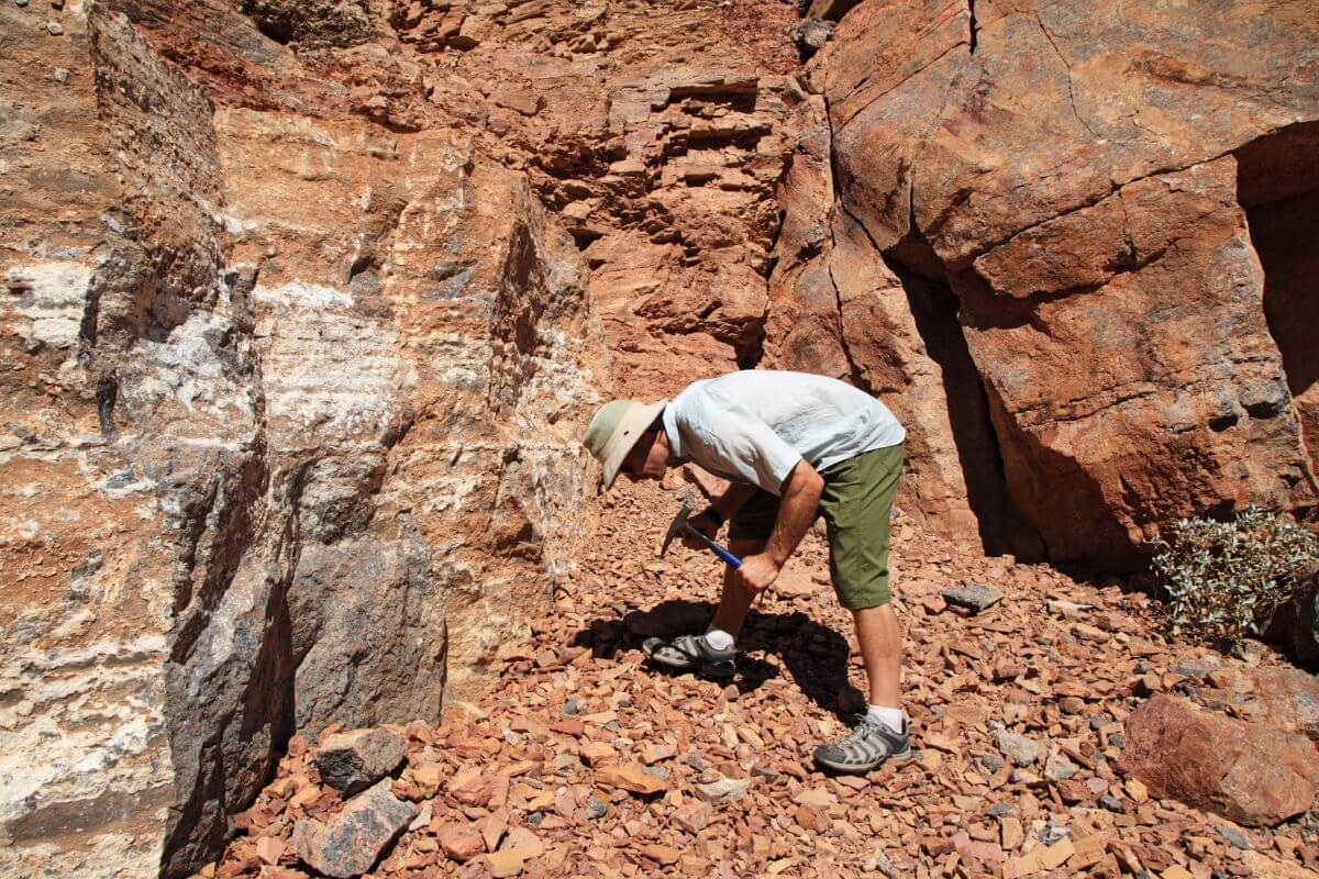 A man with a rock hammer, digging in a rocky area in Montana.
