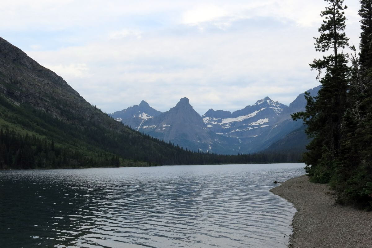 Cosley lake with rugged mountains in the distance, surrounded by dense forests under a cloudy sky.