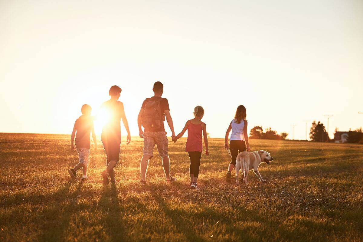 A family visiting Montana walks together in a field at sunset, enjoying their vacation.