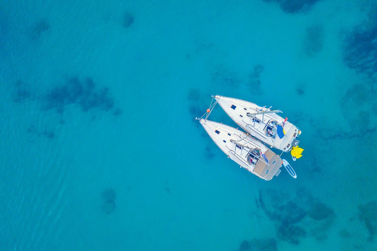 Aerial view of two boats floating on a clear turquoise sea, serving as possible major carriers of Montana invasive species.