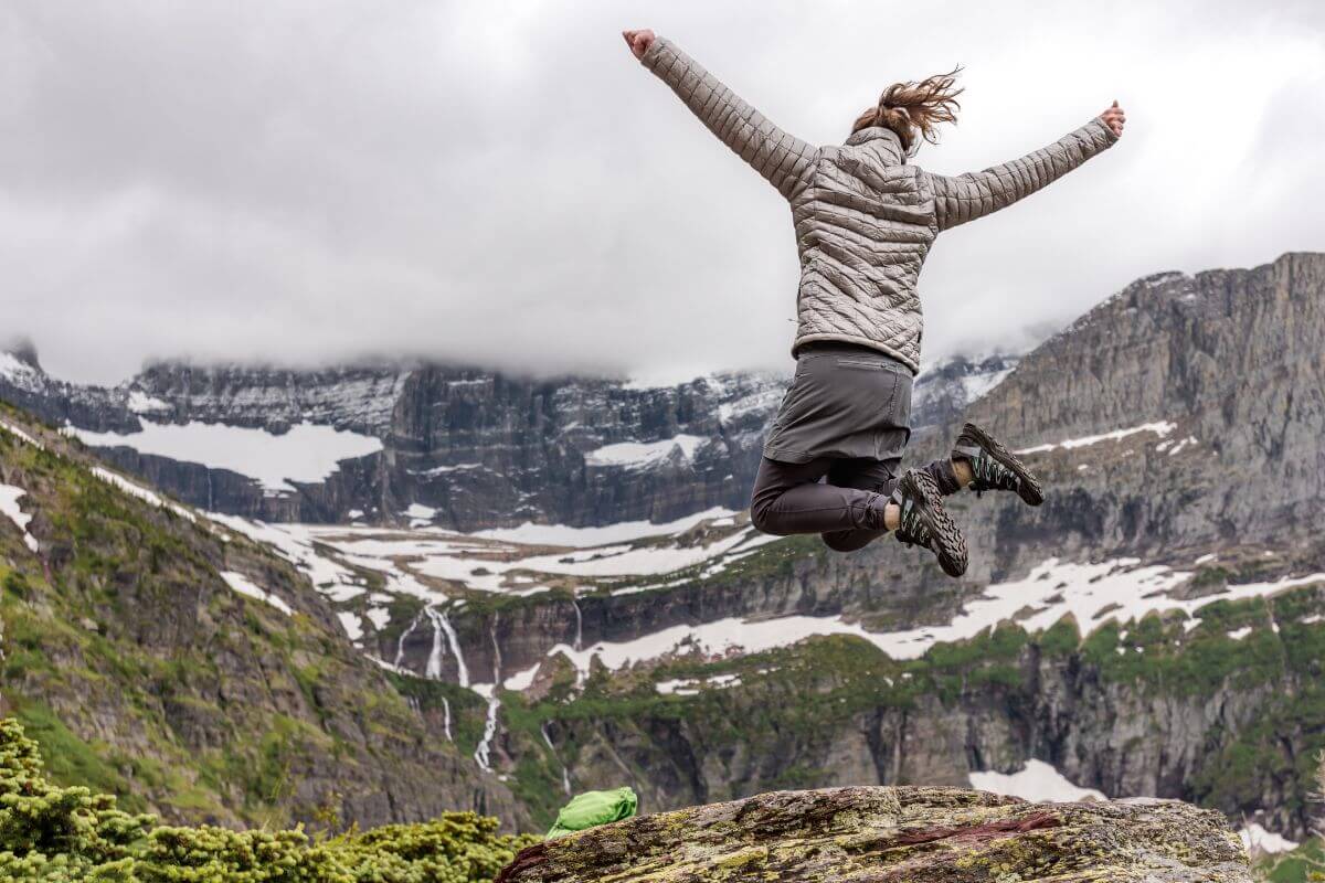 A woman is jumping on top of a mountain