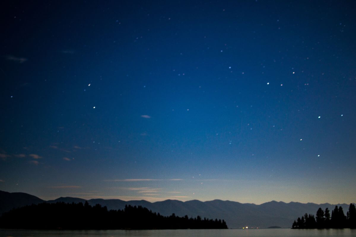 A night sky over a lake and mountains in the background.