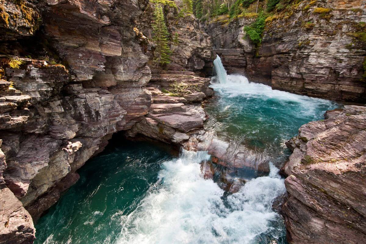 Saint Mary Falls tumbles into a turquoise pool surrounded by rugged, rocky cliffs and lush greenery.