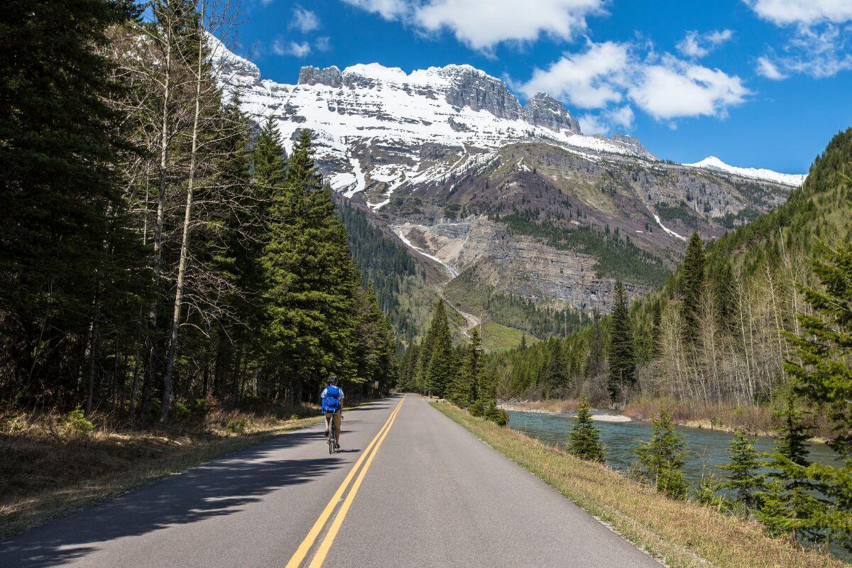 A man is riding a bike down a road with mountains in the background, showcasing one of the things to do in Montana.