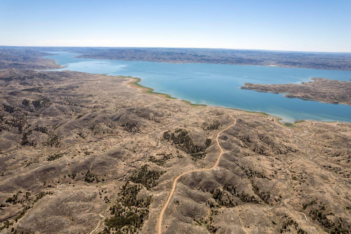 Aerial view of the American Prairie Reserve, Montana, featuring a lake surrounded by rugged terrain with sparse vegetation.