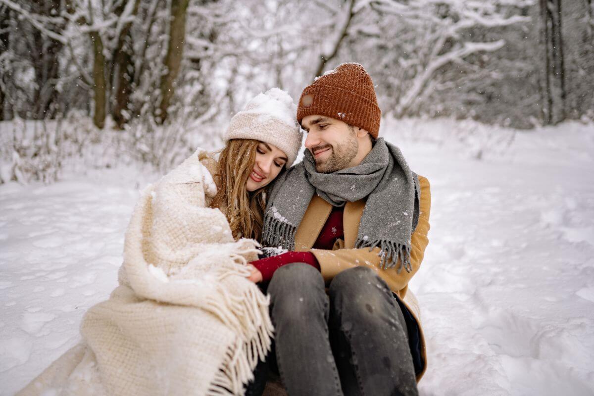 A couple, bundled up in winter clothing, sitting in the snow.