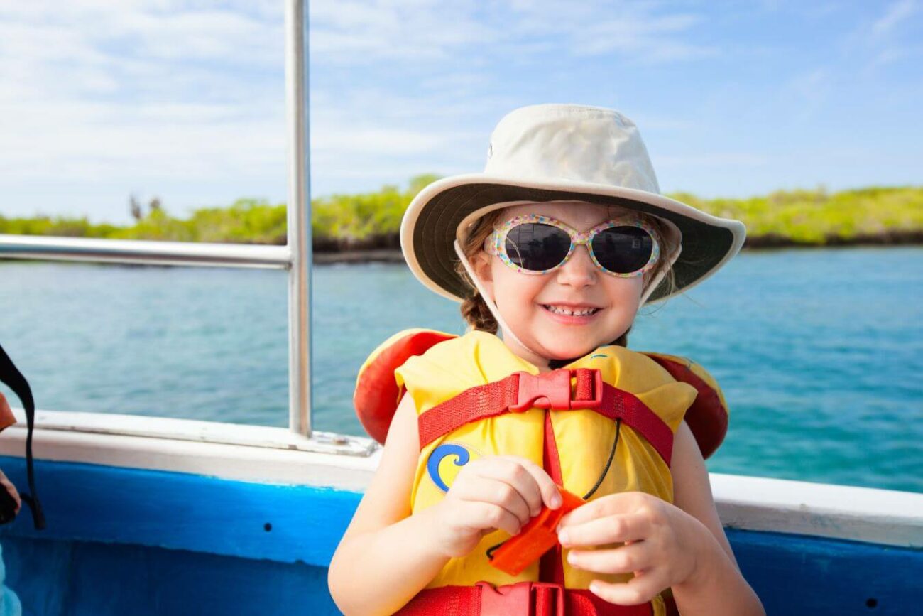 A cheerful child wearing a life jacket, hat, and sunglasses smiles aboard a boat in Montana 