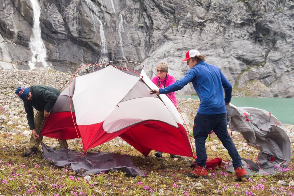 Three people are pitching a red tent in a mountain landscape near Monture Waterfall