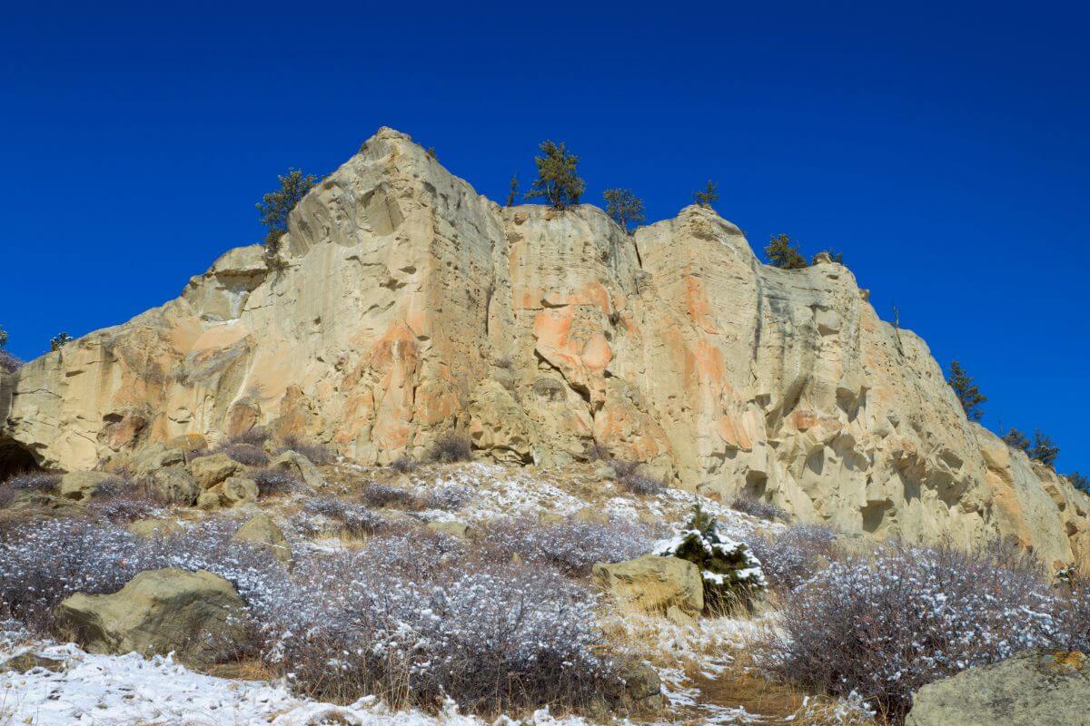 Rock formation amid the pristine snowscape, complemented by a striking backdrop of towering trees at Pictograph Cave State Park, Montana.