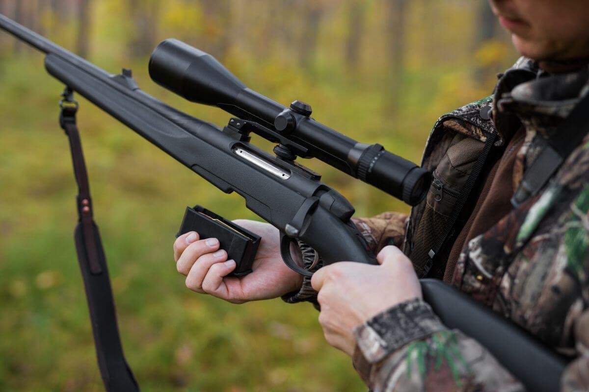 A person in camouflage clothing loading a magazine into a bolt-action rifle with a scope in Montana