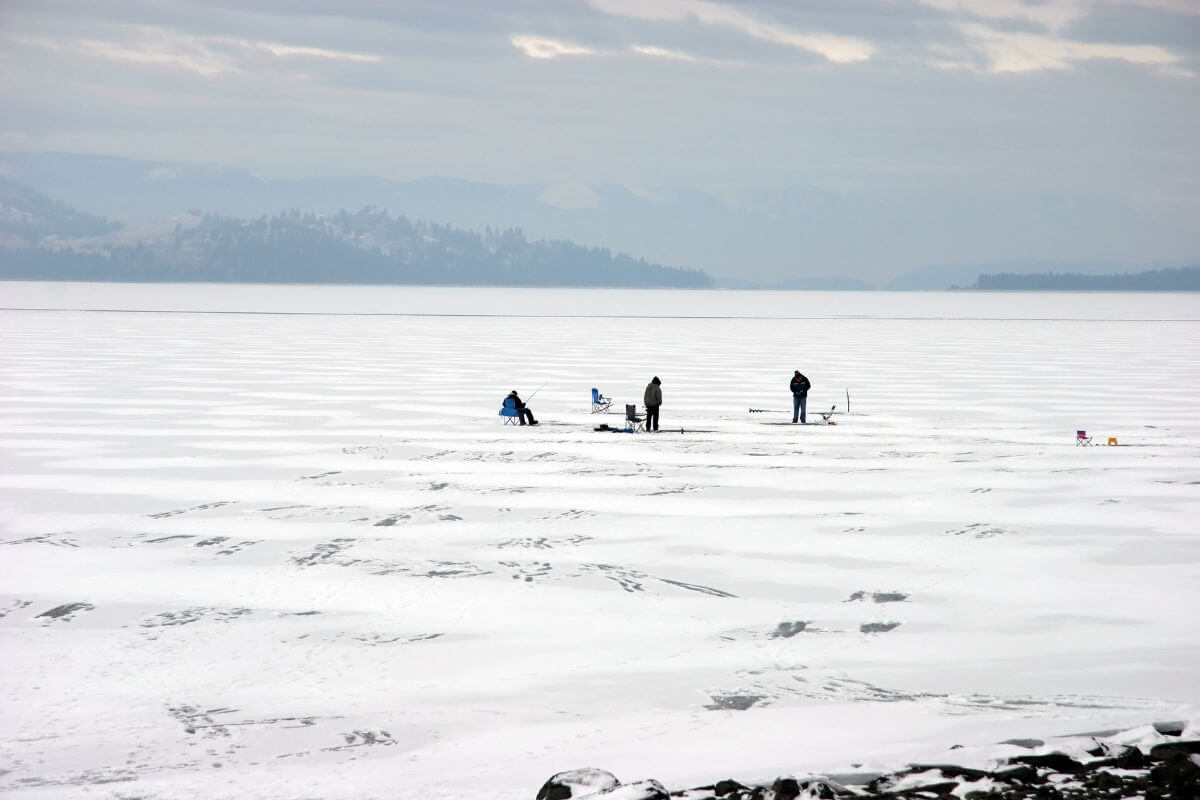 A group of people fishing in the snow on a frozen lake in Montana during February.