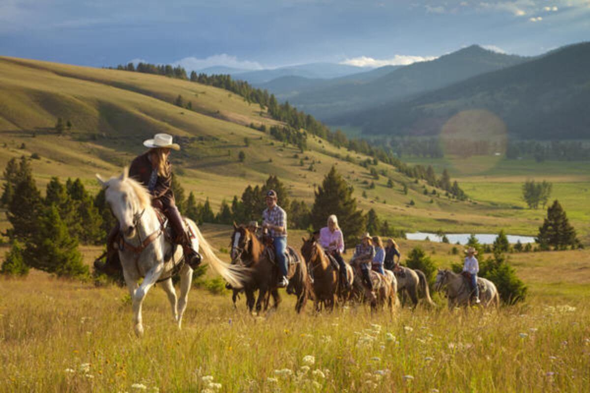 A group of people riding horses in a field in Montana during fall.