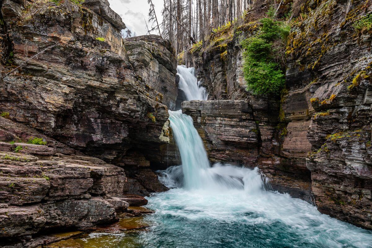 A waterfall in the middle of a rocky canyon in Glacier National Park.