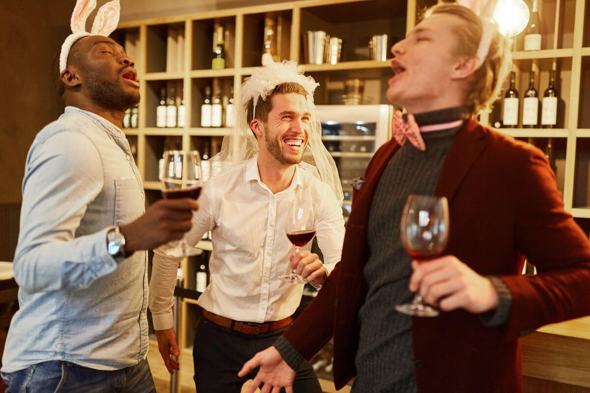 Two men in bunny headbands and a man with a wedding veil drinking wines in a bar in Montana during their bachelor party.
