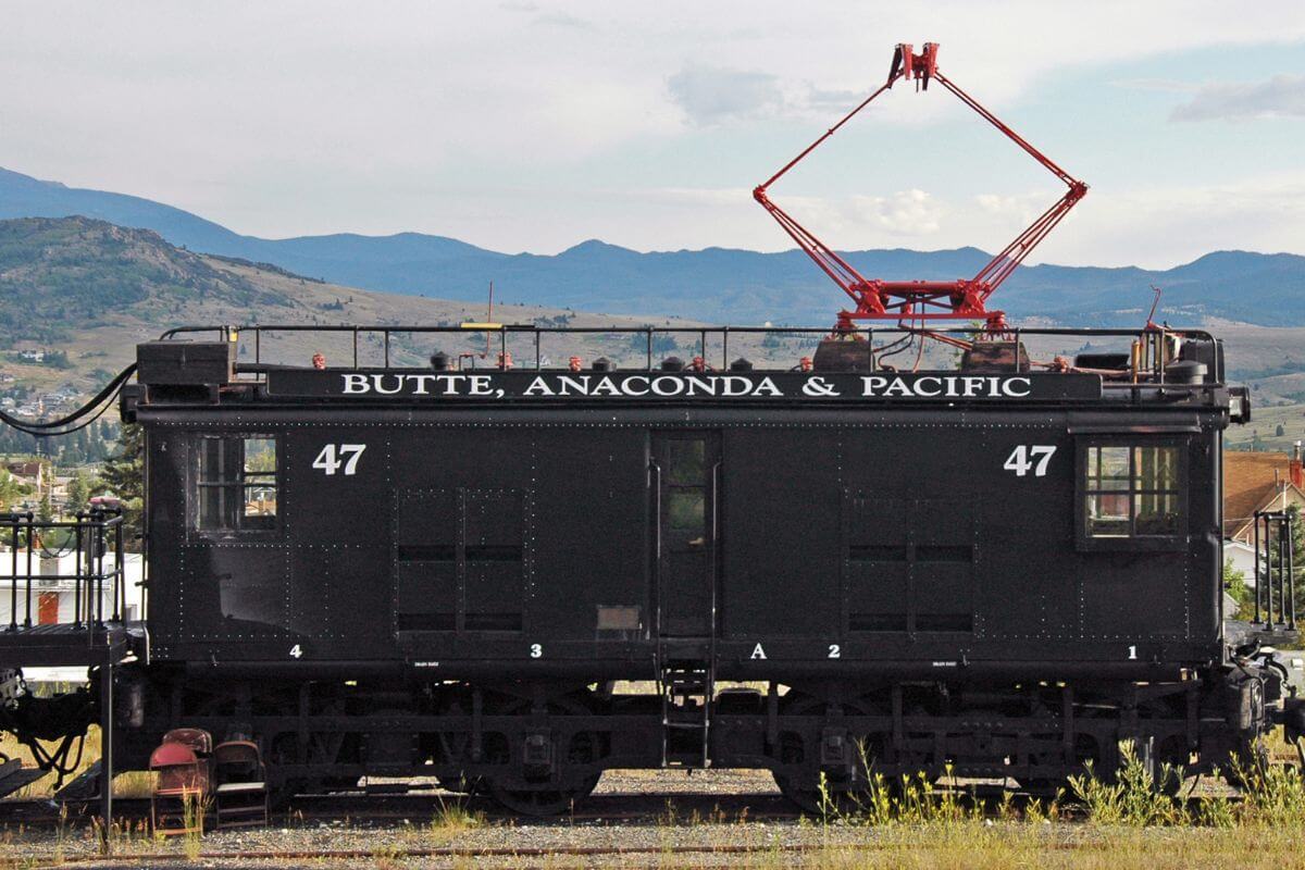 A black train car on the tracks with mountains in the background in Montana.