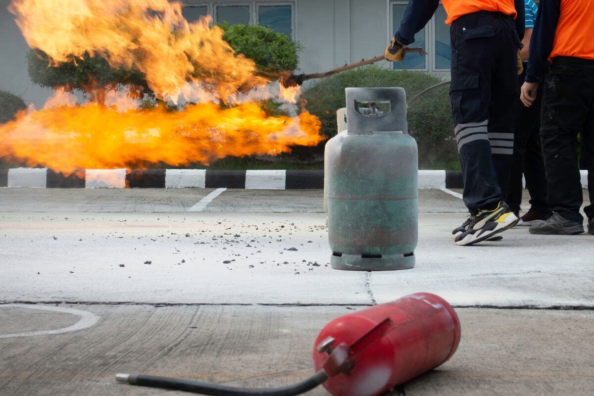 Three individuals standing close to gas tanks in the middle of fire extinguisher training in Montana, with one of them holding a burning branch.