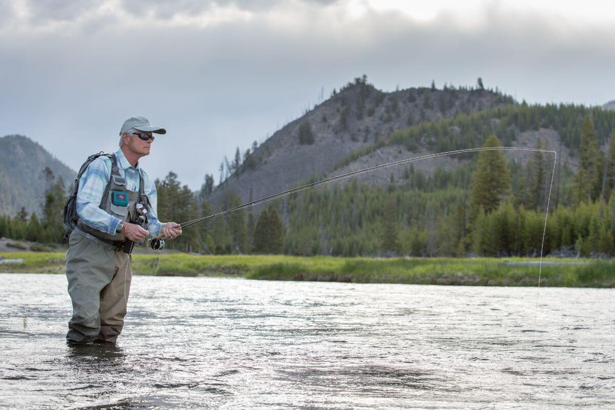 A man is fly fishing in a river with mountains in the background in Montana.