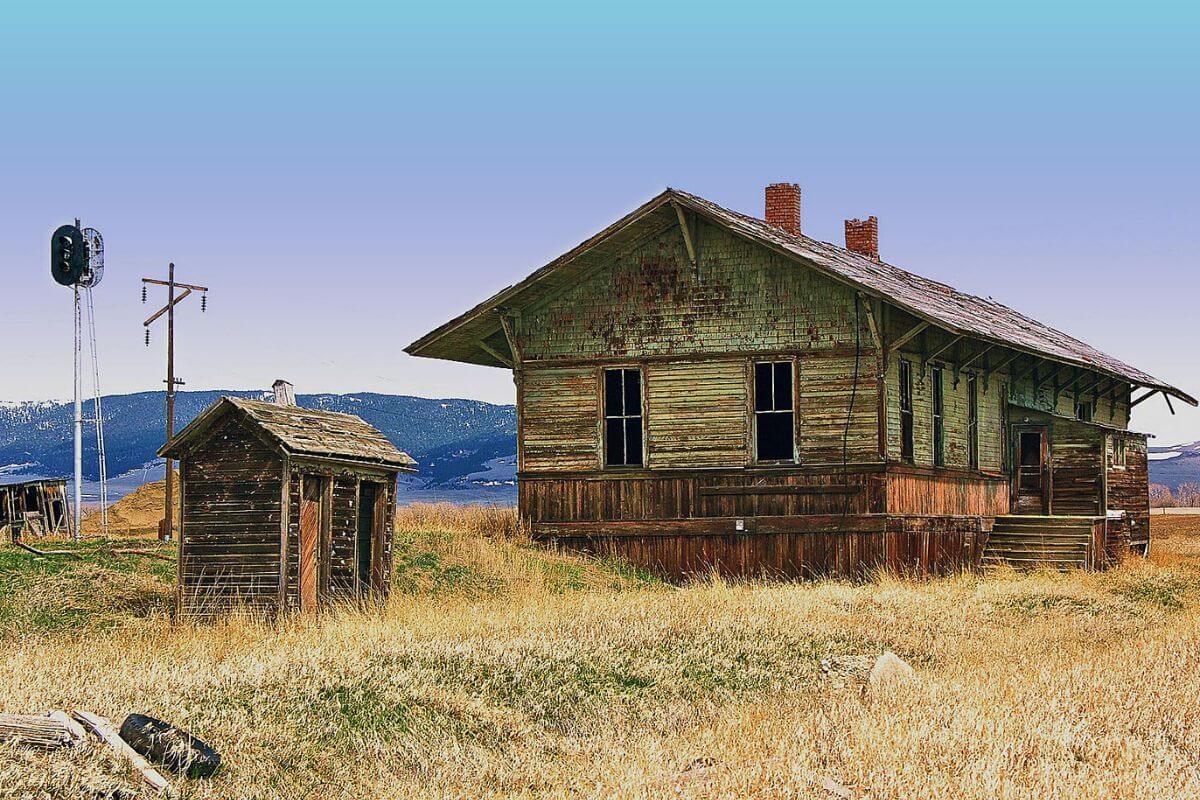 An old abandoned wooden building and a shed lie in a grassy field in Montana