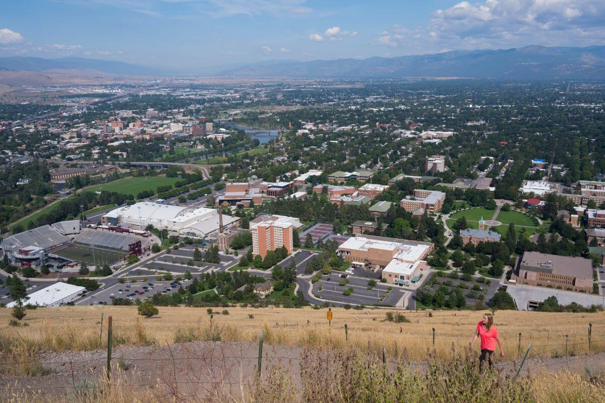 A woman is walking on a hill overlooking a Montana city, with mountains in the distance.