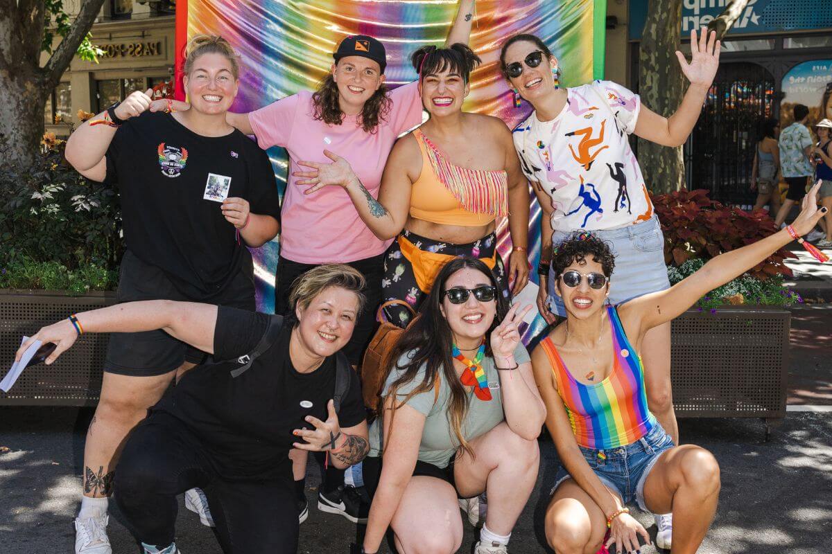 A group of women posing for a photo in front of a rainbow banner