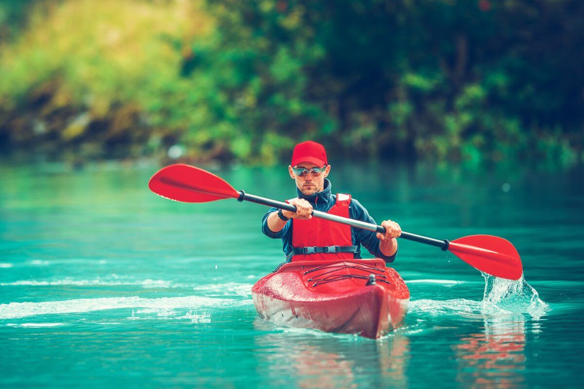 A man in a red kayak paddling down a river in May.