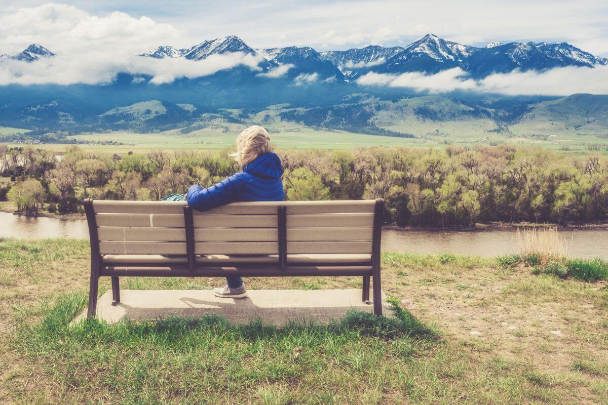 A woman sits on a bench, peacefully retiring in Paradise Valley, Montana, while overlooking a breathtaking river and mountains.