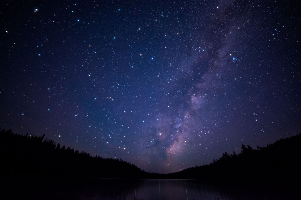Stars shimmer in the night sky over a lake.