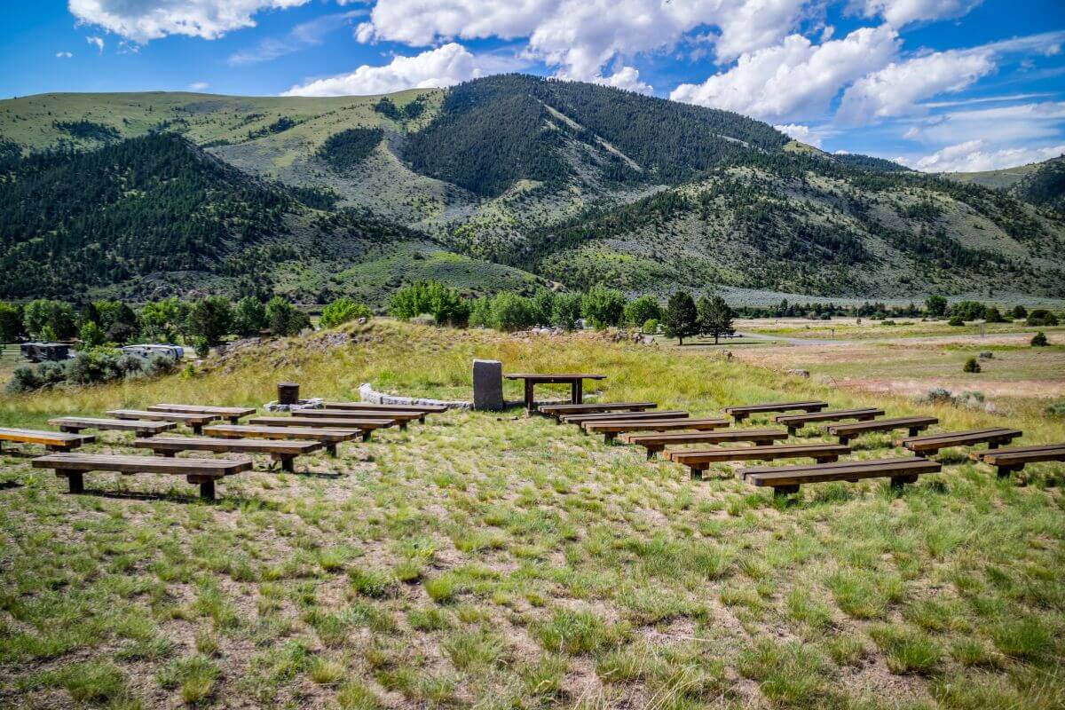 A row of benches is set up in a grassy field with mountains in the background at Lewis & Clark Caverns State Park, Montana.