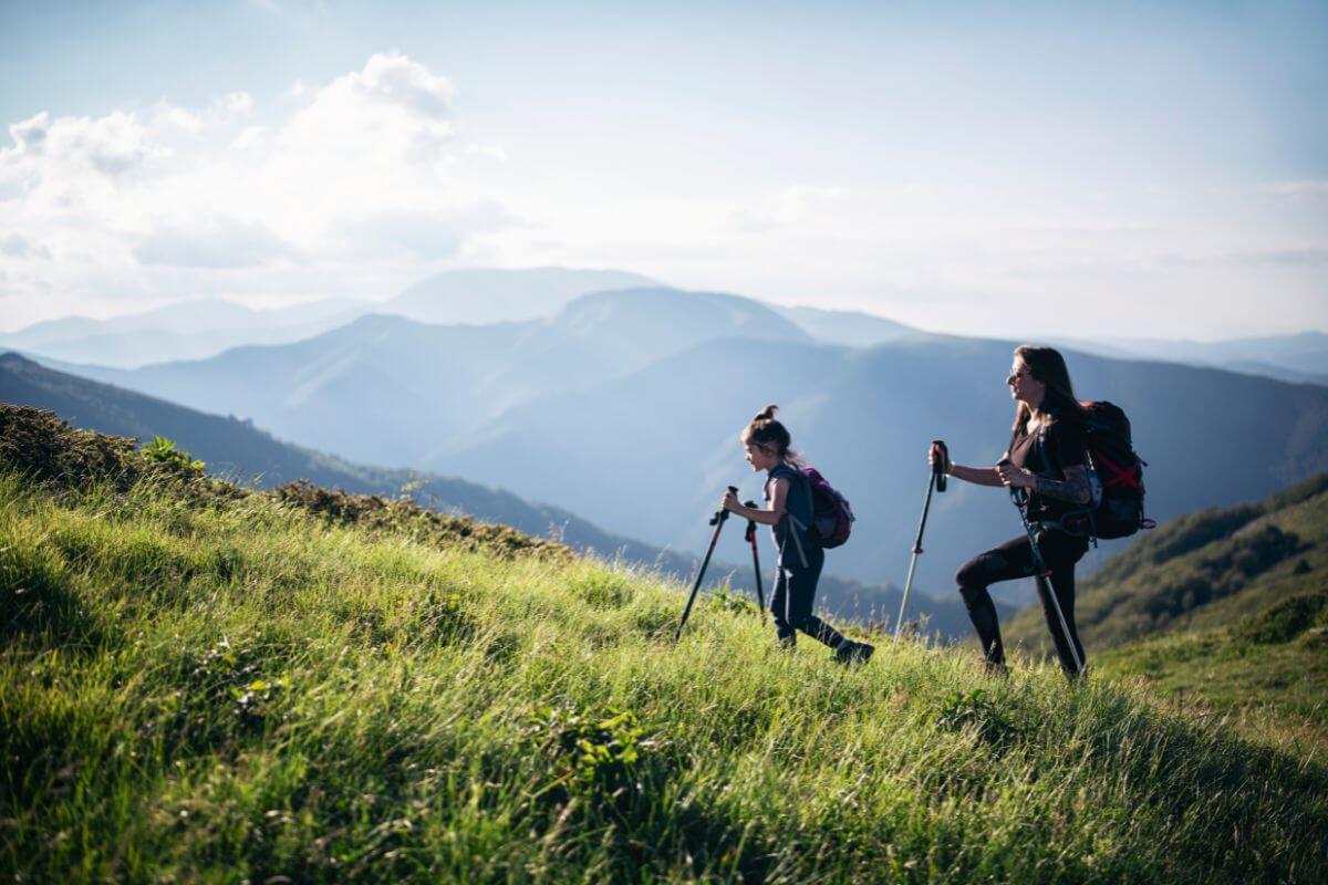 A mother and daughter trek up a grassy mountainside during their Montana tour expedition.