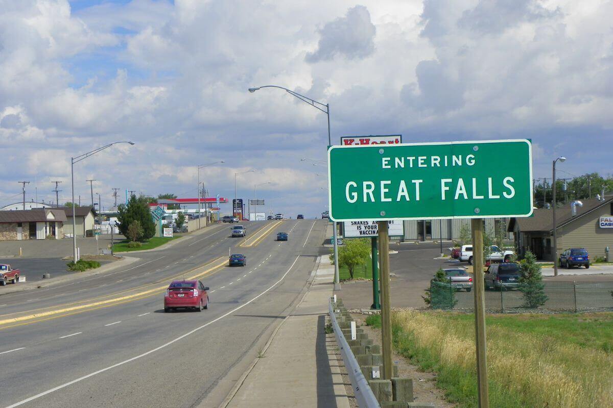 A green and white sign with the words "Entering Great Falls" on the side of a road.