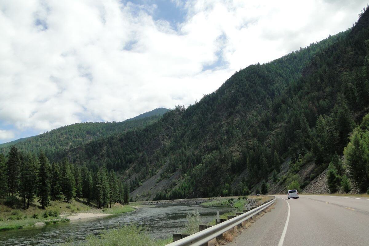 A car driving down a road next to a river and a mountain in Montana.