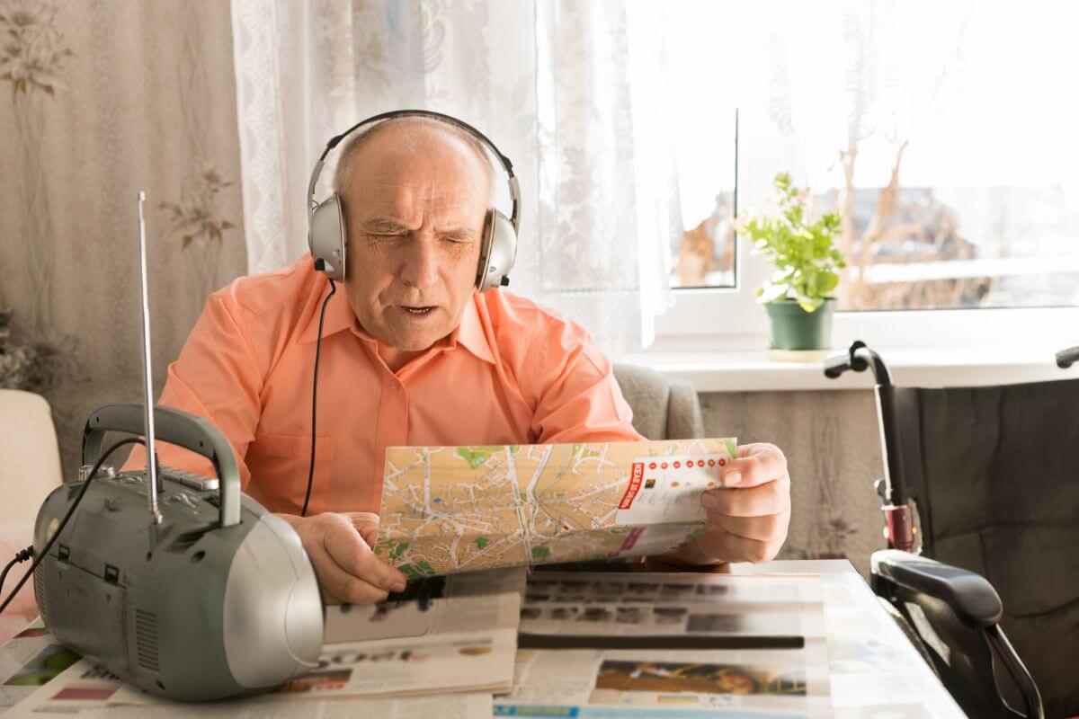An elderly man is listening to a radio with a map in hand, preparing for a Montana flood.