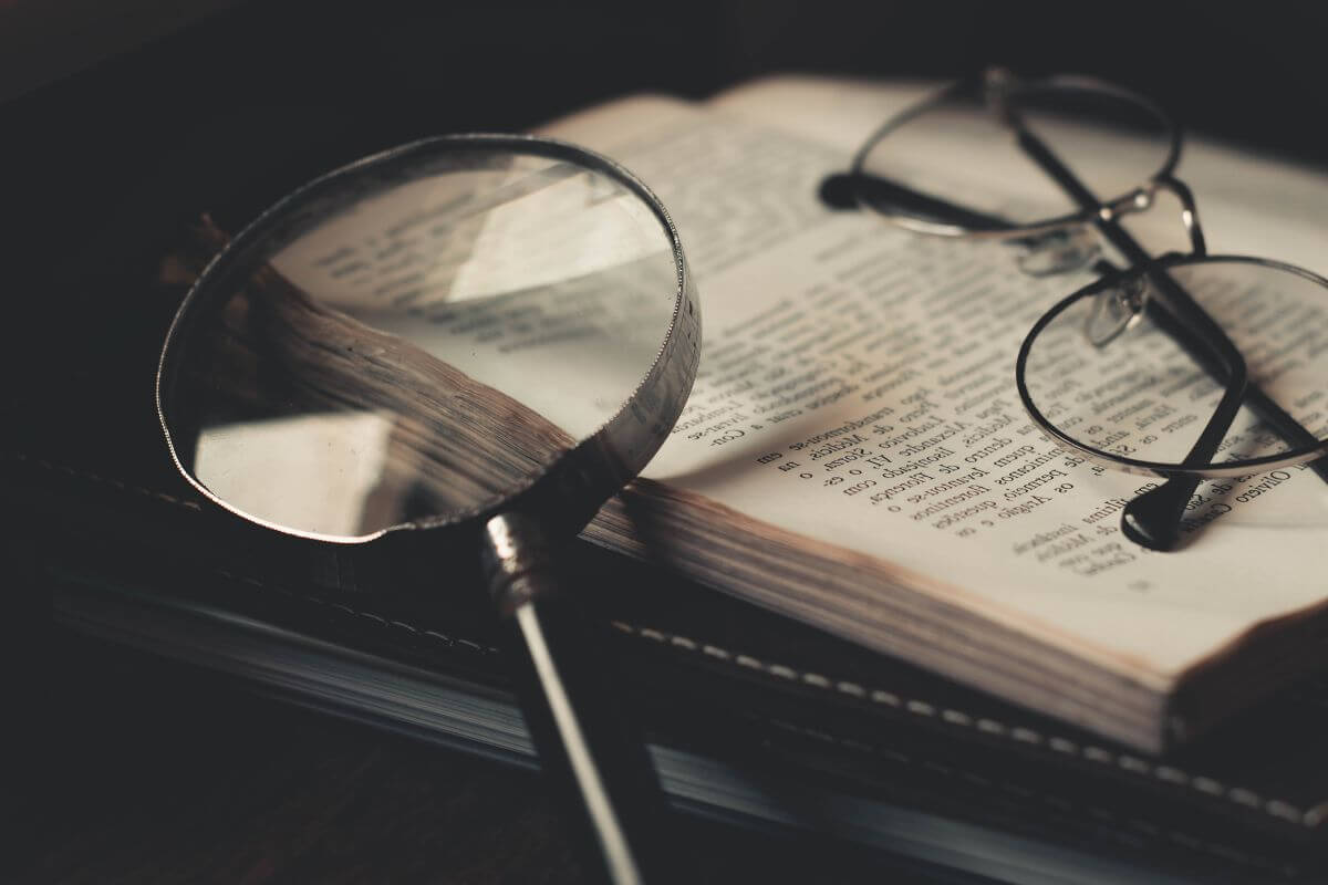 A pair of glasses and a magnifying glass sit on top of an open book