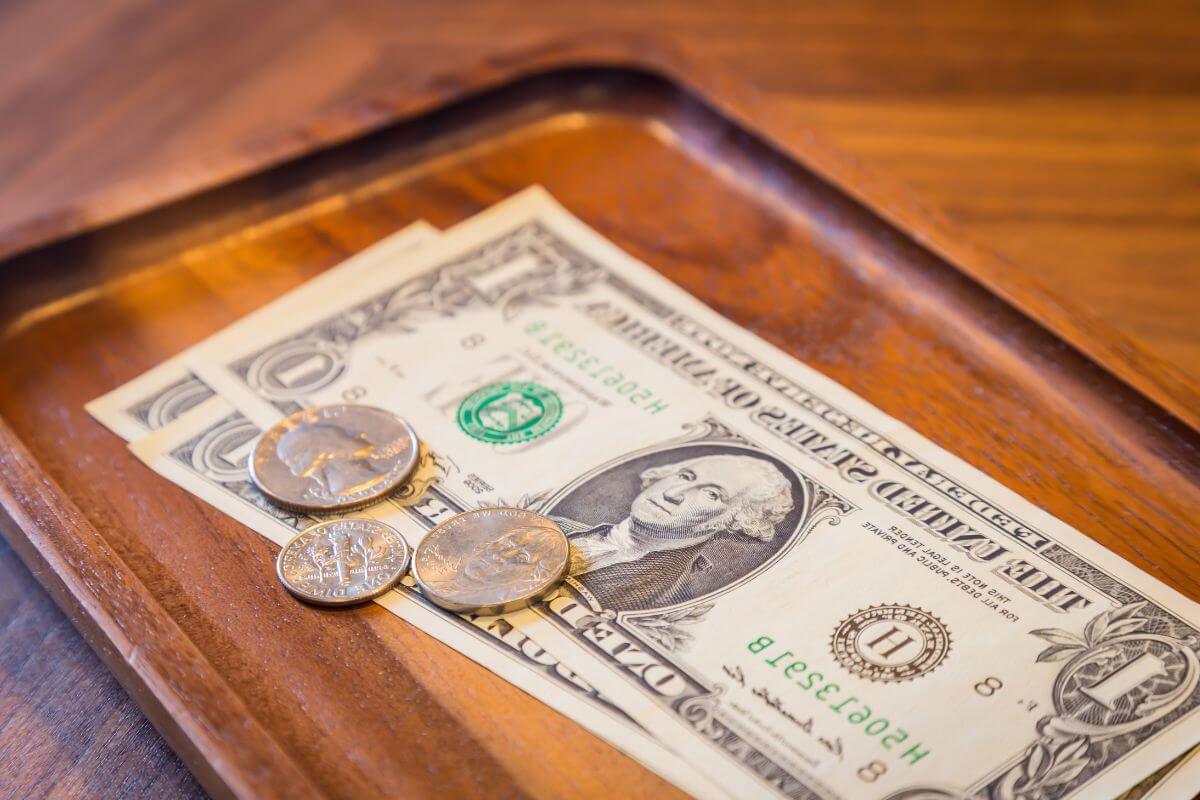 A wooden tip tray with a couple of dollar bills and coins.
