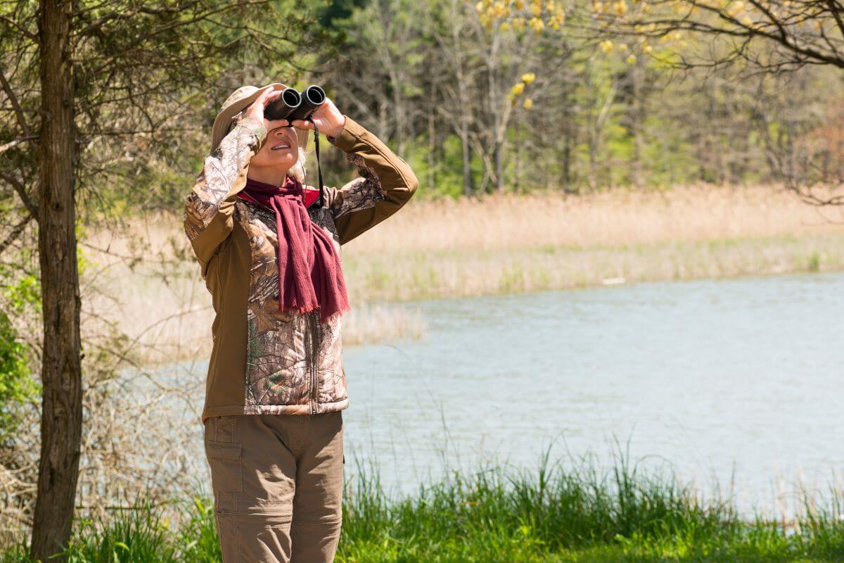 A woman, near a pond in Montana using binoculars to observe birds