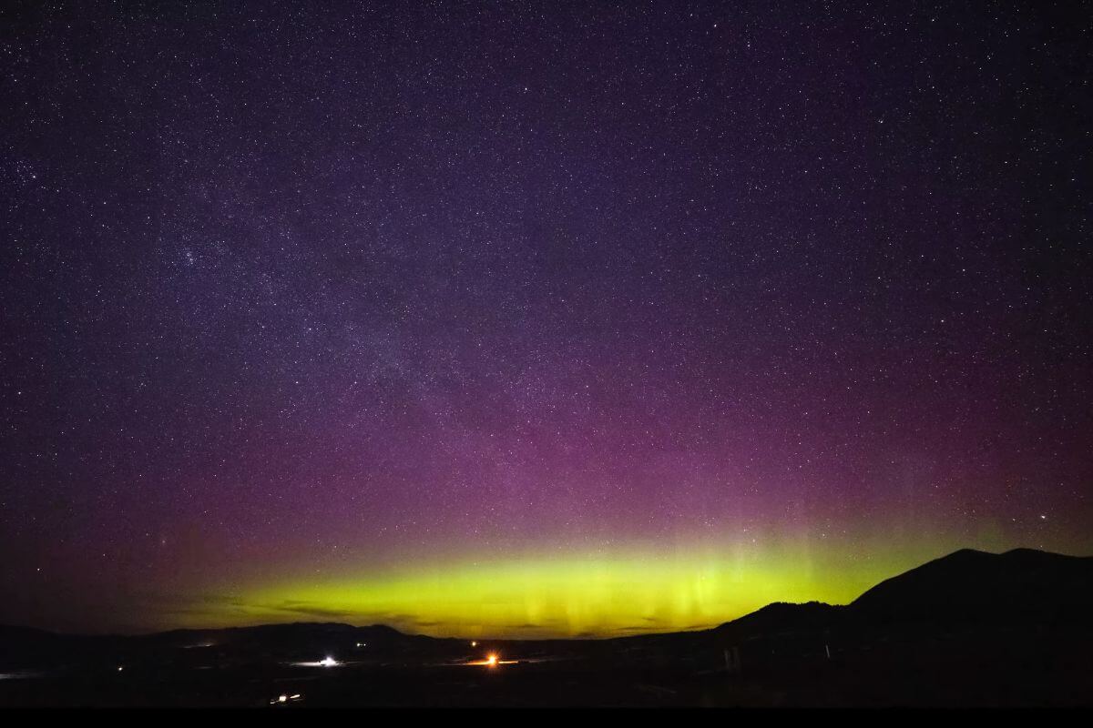 An aurora borealis lights up Montana's starry night sky in green and purple hues. 
