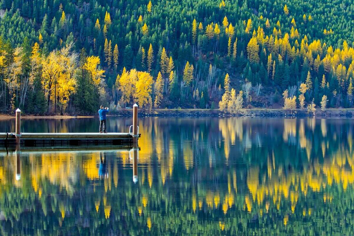 A man stands at the edge of a dock on a lake surrounded by trees in Montana.