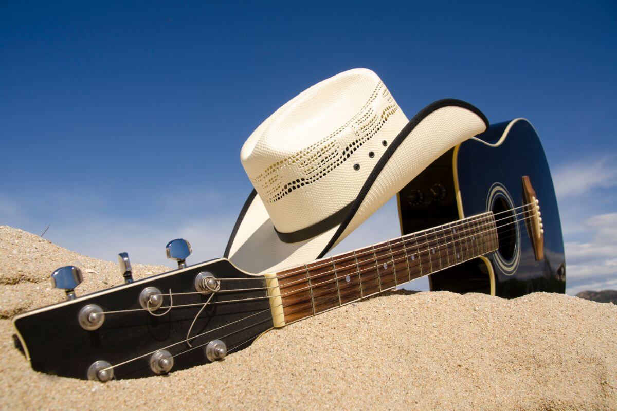 An acoustic guitar laying on the sand with a cowboy hat in Montana.