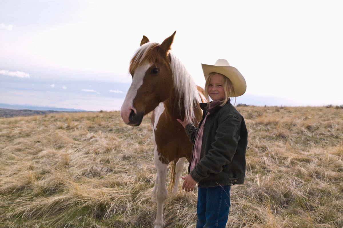 A girl in a cowboy hat standing next to a horse in Montana.