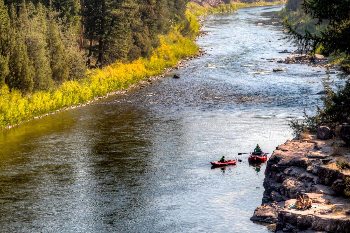 Two people sitting down on the rocks and two people kayaking on the Blackfoot River, Montana.