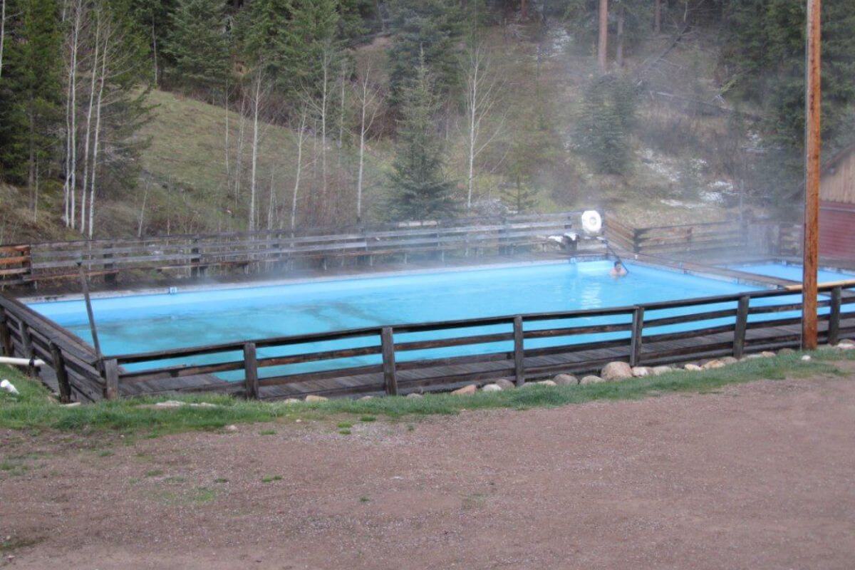 A person enjoys a solitary dip in the steaming pool, surrounded by a wooden fence, at Elkhorn Hot Springs in Montana.