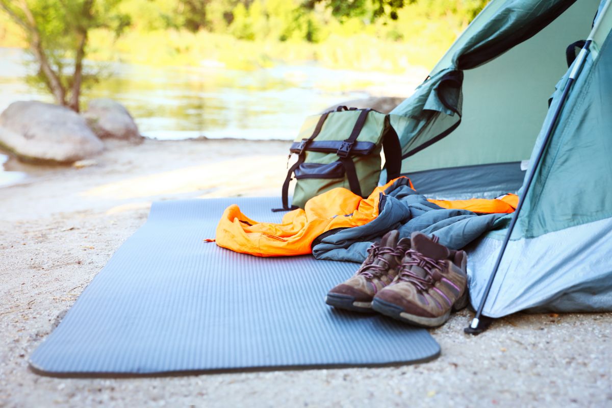 Campsite by a river near Mill Falls with an open tent, sleeping bag, mat, backpack, and hiking boots laid out in a sunny natural setting.