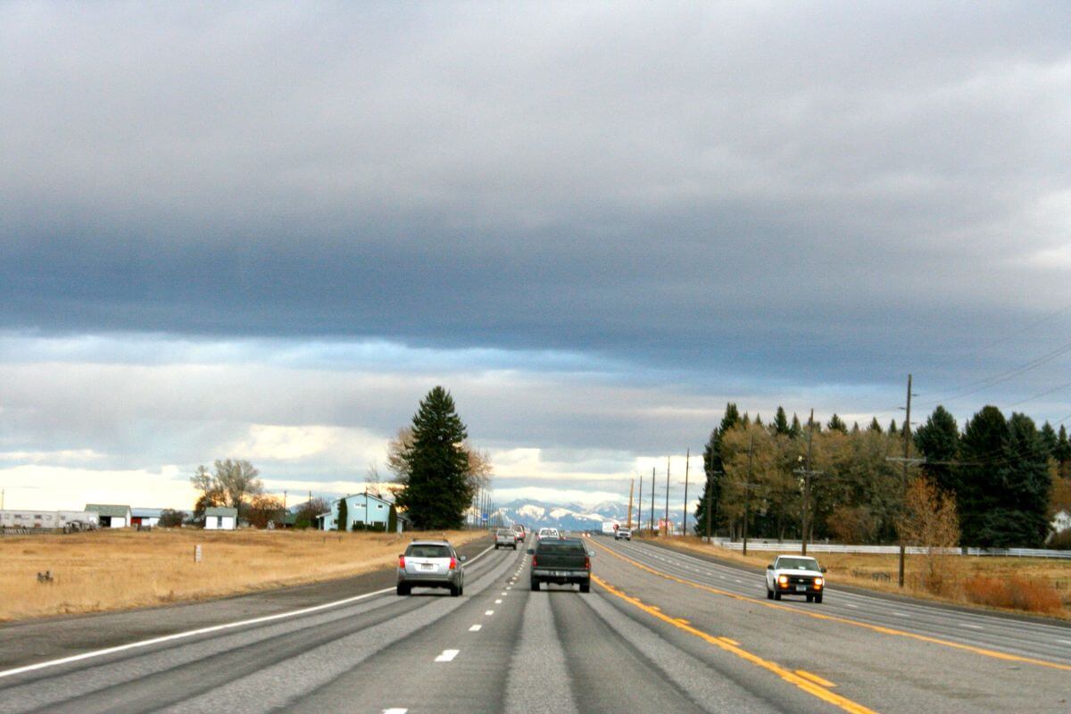 Cars drive along a calm Montana highway during a cloudy day.