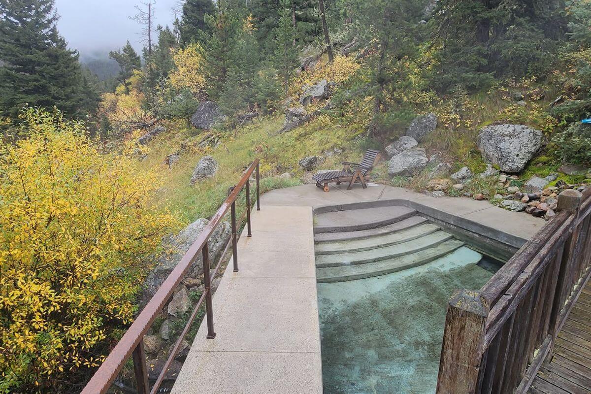 The Potosi Hot Springs pool in the mountains, enclosed in a steel barricade, features steps and a wooden bridge