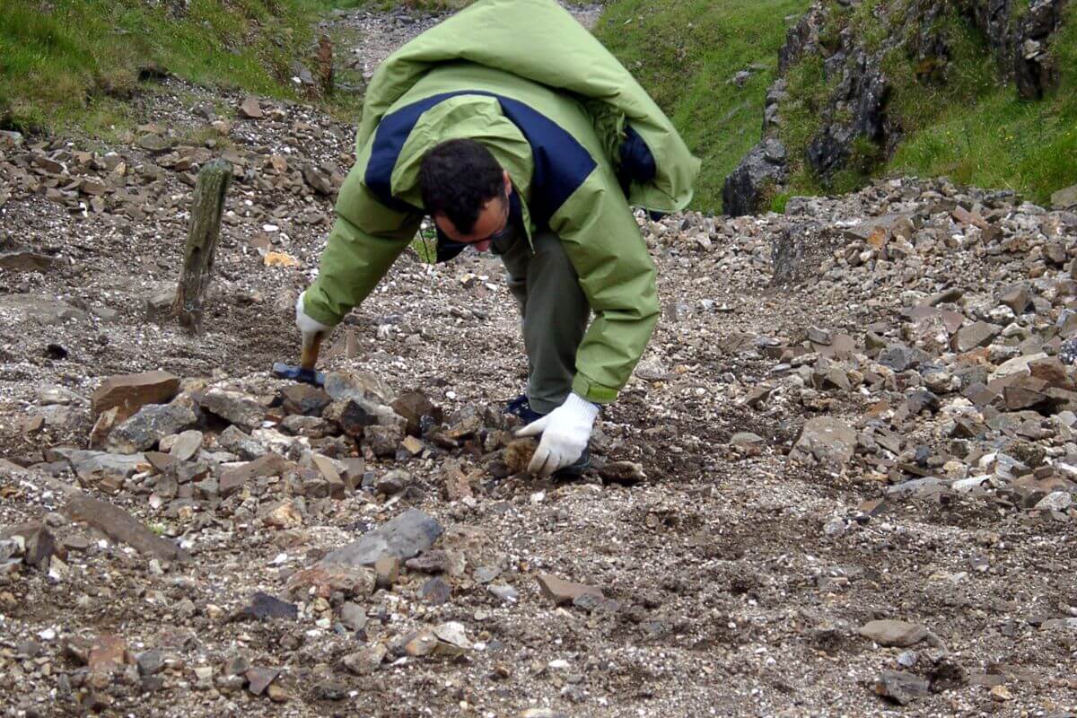 A man rockhounding in Montana, wearing a green jacket and digging through rocks.