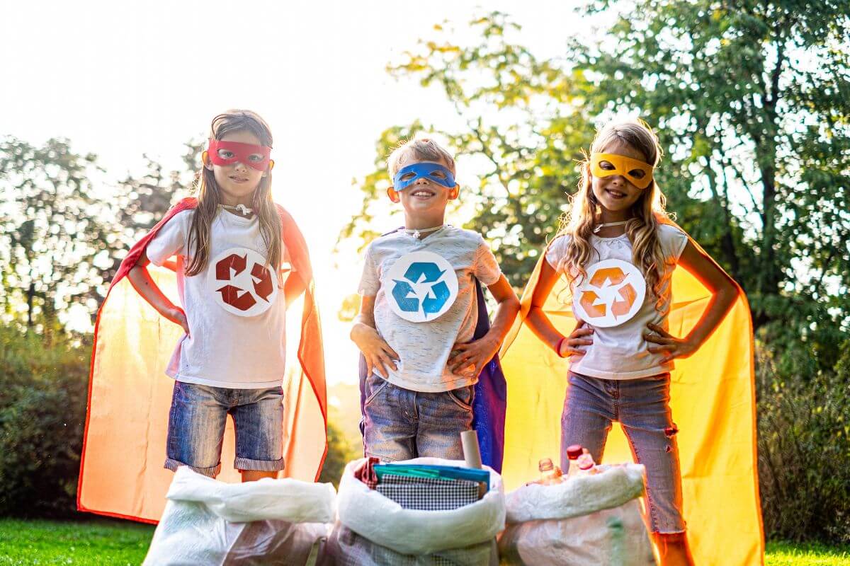 Three kids in superhero costumes next to trash bags