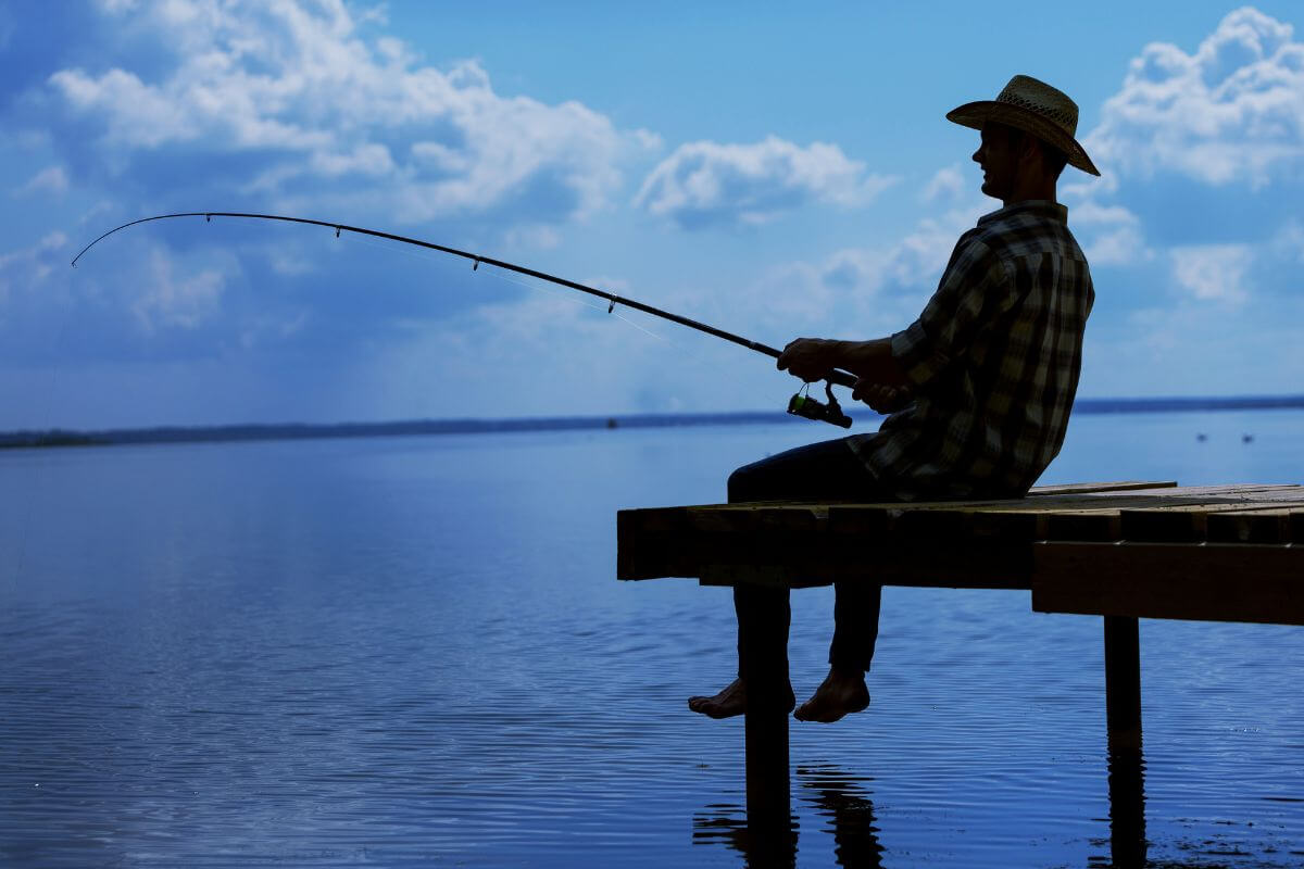 A silhouette of a man sitting on a wooden dock, fishing with Montana's Aquatic Invasive Species Prevention Pass.